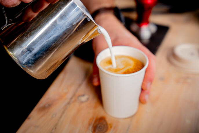 Pouring premium barista-made coffee, one cup at a time. A barista pouring steamed milk into a white paper cup to create latte art.