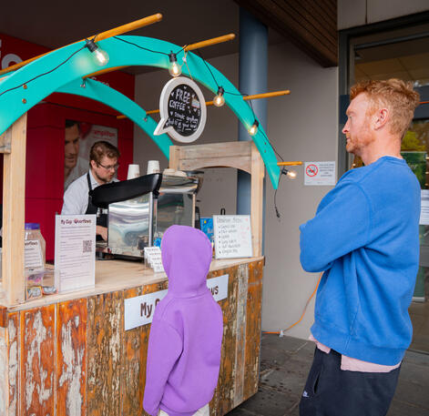 Family-friendly catering that brings a smile to guests of all ages. A man in a blue sweater and a child waiting at a wooden coffee cart.